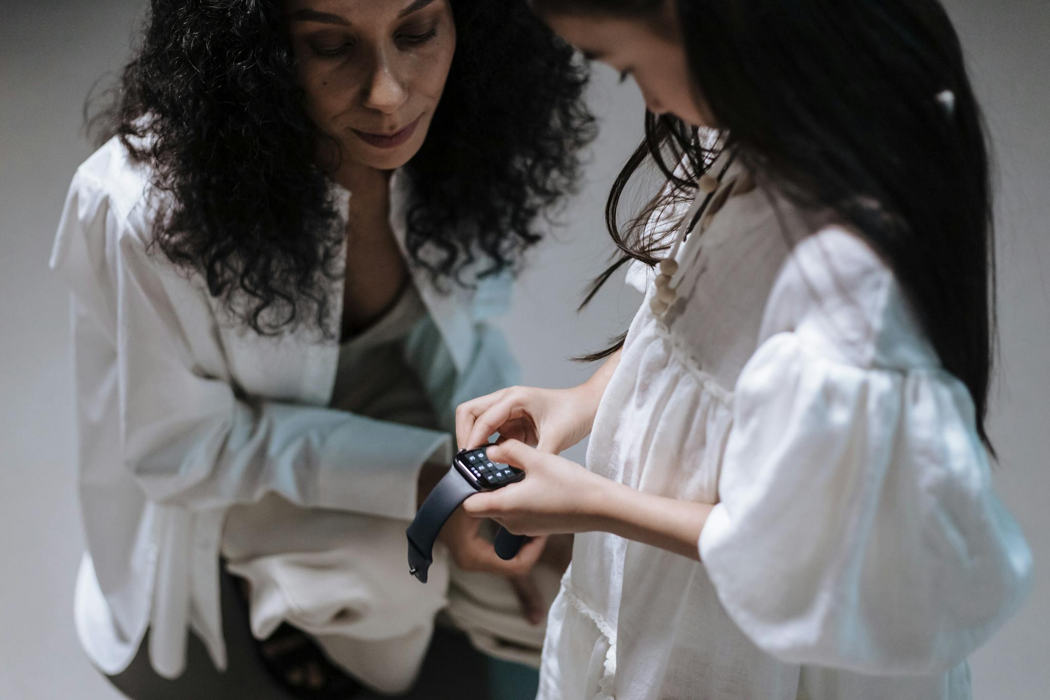 A mother and daughter interact with a smartwatch, showcasing family bonding with modern tech.